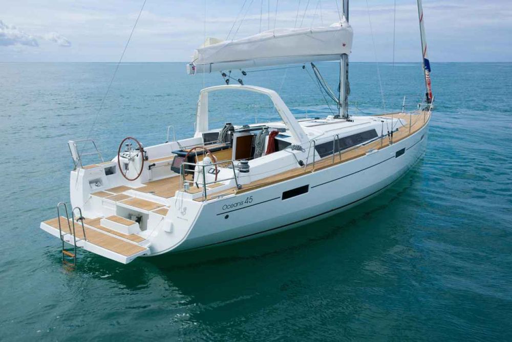 A modern white sailboat, the Oceanis 45, floating on calm turquoise water under a partly cloudy sky, with an open cockpit and sleek deck design.